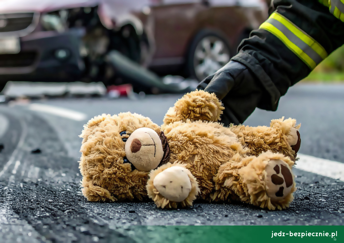 Wypadek drogowy z udziałem dziecka, leżący miś pluszowy na jezdni, którego podnosi strażak